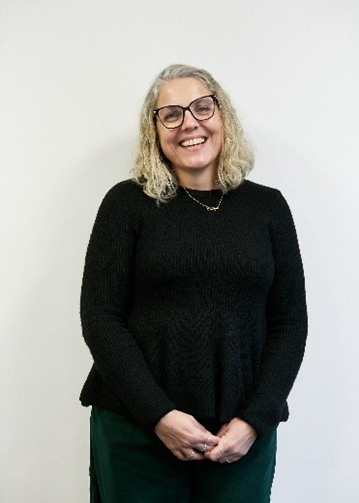 Jacqui Kempen, a white woman with long blonde hair, wearing glasses, a black top and dark green trousers
